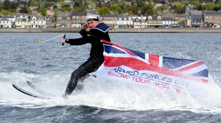 Sailor jet skiing with Armed Forces Week flag