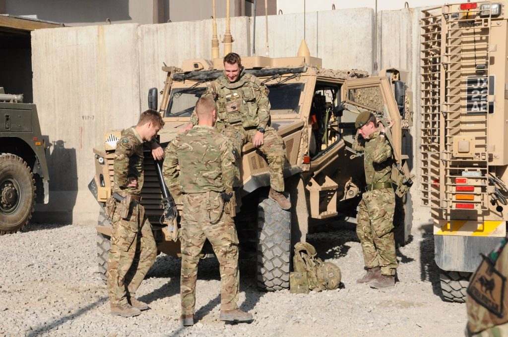 four reserves chat while standing around an army vehicle against a Kabul backdrop.