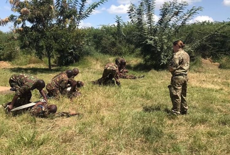 Female reserve in British Army uniform teaches Kenyan soldiers some first aid techniques.