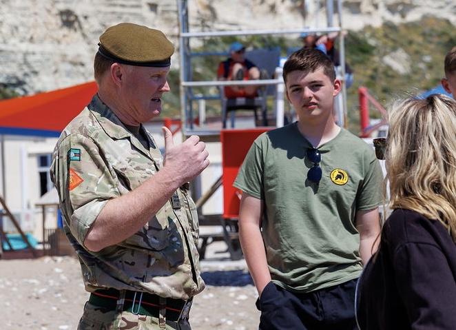 Man in uniform talks to some young people on a beach