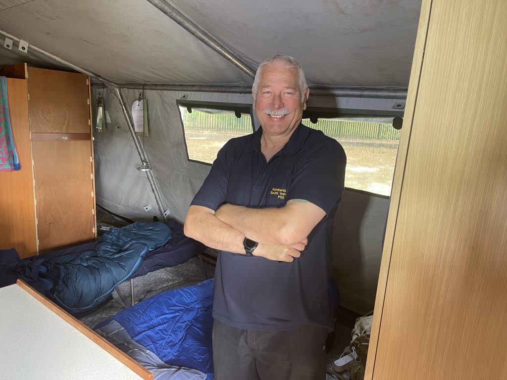 Man inside tent with beds behind and furniture