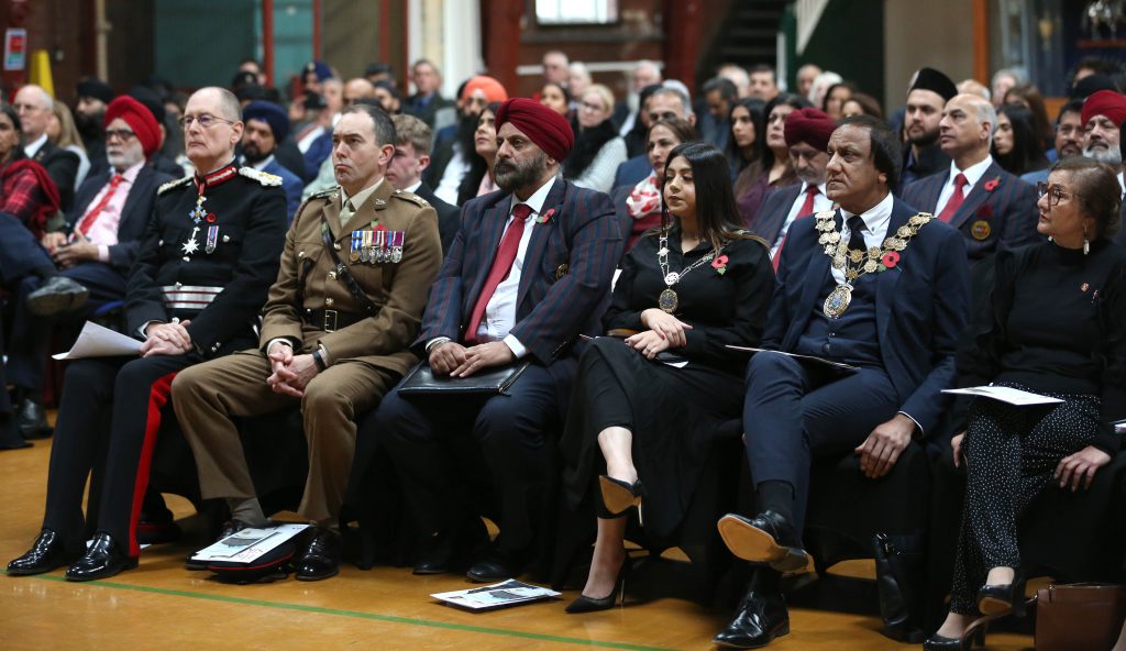 Men and women in military uniform or sombre attire wearing poppies and chains of office
