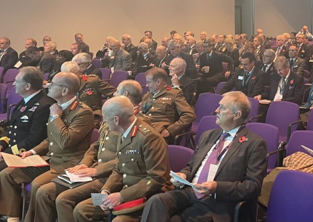 An auditorium of white men - those at the front in military uniform - facing the stage