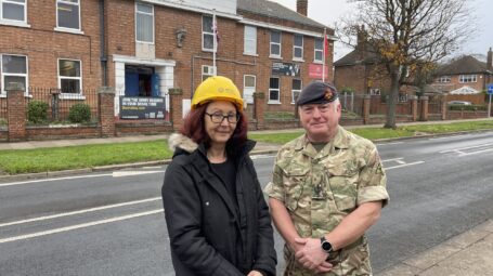Woman in an RFCA hard hat together with a man in a reserve uniform in front of a barrack-style building