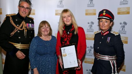 Four people in a line, one of whom is holding a certificate and two are in military uniform