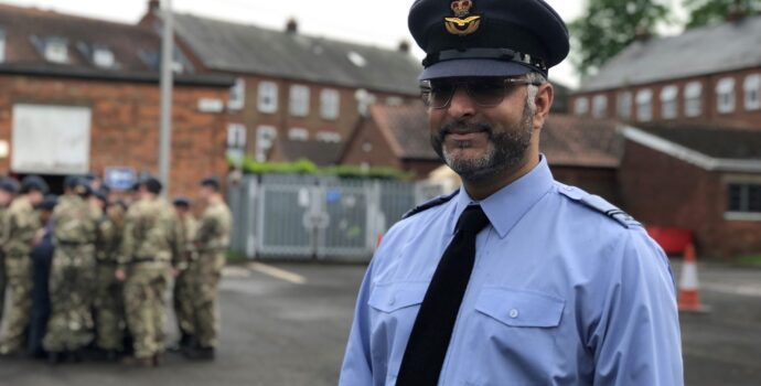 Cadet force adult volunteer, Zia Mir, standing in his uniform with a group of air cadets in the background