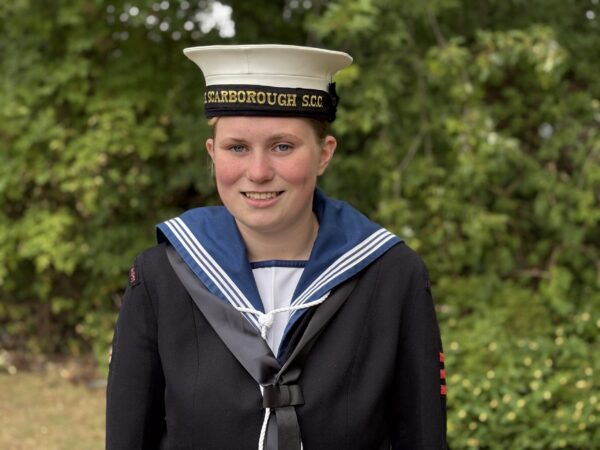Sea Cadet Izzy Parkins in her uniform stands in front of shrubbery