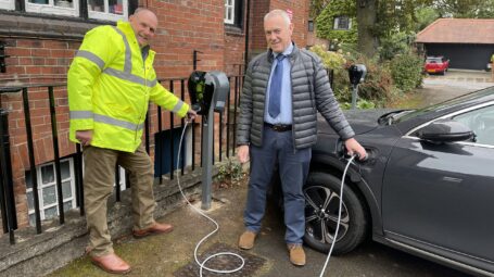 Man in hi visibility jack with a man filling a car from an electrical charging point