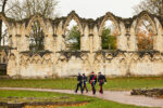four people in uniform walk along a path with the ruins of an abbey in the foreground