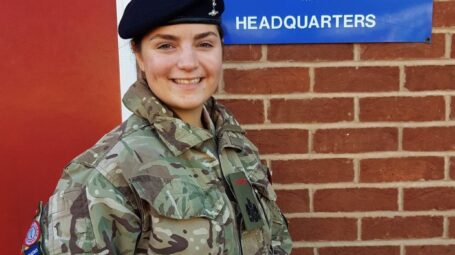 An army cadet standing in front of a building with a trophy in her hands
