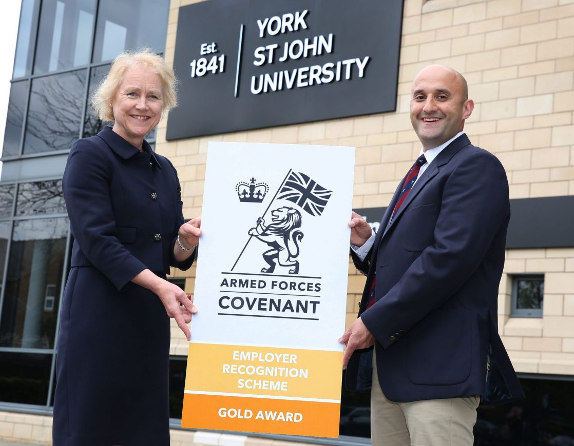 Woman and man holding a Gold Award banner outside York St John University